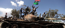 Rebeldes libios ondean la bandera tricolor sobre un tanque calcinado.